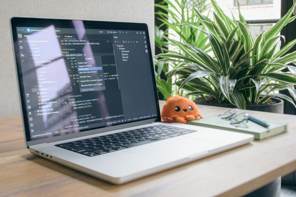 A modern home office setup featuring a laptop with coding software, a plant, and a plush toy.