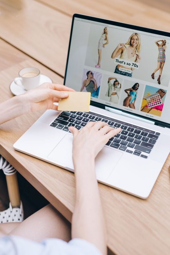 Hands holding a credit card while online shopping on a laptop at a wooden table.